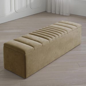May include: A rectangular, beige storage bench with a ribbed, padded top. The bench is made of a textured fabric and sits on a light-colored wooden floor. The bench is a neutral color and would fit in many home decor styles.