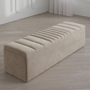 May include: A beige rectangular storage bench with a ribbed, padded top. The bench is made of a textured fabric and has a hinged lid for storage. The neutral color and simple design make it suitable for various interior styles.