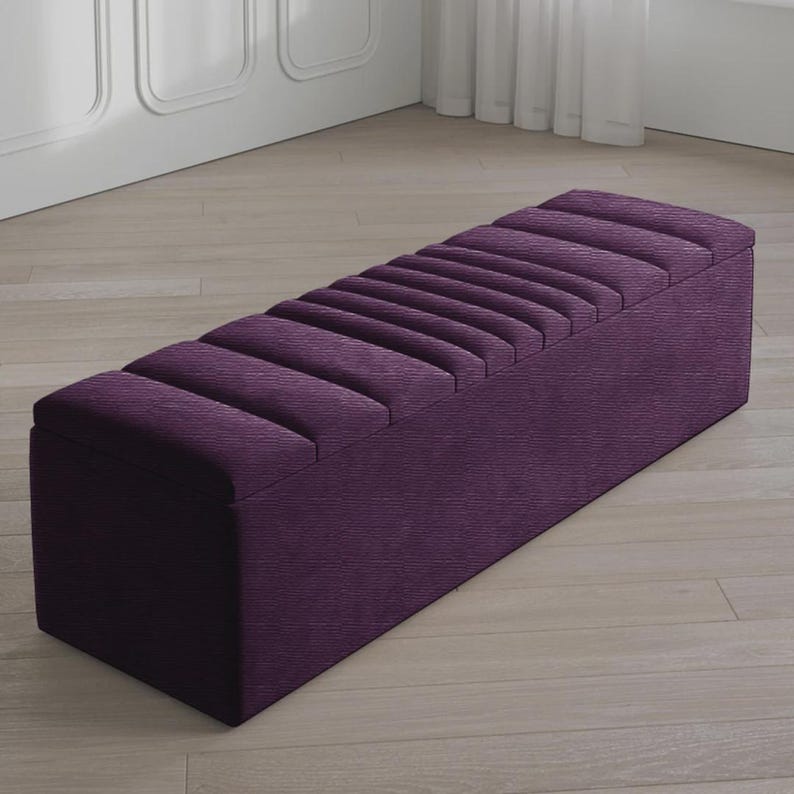May include: A rectangular, purple upholstered bench with a ribbed top. The bench is a deep shade of purple and has a clean, modern design. It is placed on a light-colored wooden floor.