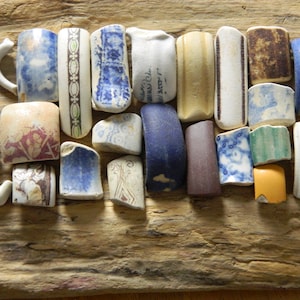 May include: A selection of ceramic fragments, including mug handles and decorative tiles, in blue, white, brown, and yellow hues. The pieces are displayed on a weathered wooden surface, with diverse patterns and textures.