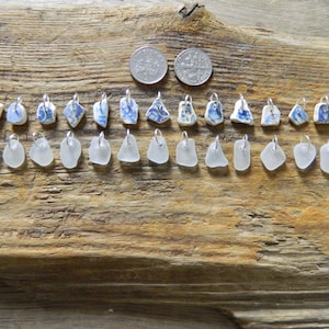 Può includere: Una collezione di piccoli ciondoli, alcuni con pezzi di ceramica a motivi blu e bianchi e altri con vetro trasparente smerigliato. I ciondoli sono esposti su una superficie di legno stagionato, con due monete in alto.