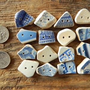 May include: Sixteen irregular ceramic buttons with two holes each, featuring various blue and white patterns. Two circular metal coins are placed to the left for scale, with one coin showing the text 'United States of America' and 'One Dime'.
