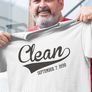 Puede incluir: Camiseta blanca con texto negro que dice "Clean" en una fuente de béisbol vintage. Debajo del texto está "SEPTEMBER 7, 1998". El sitio web "WoodenUrecover.com" está impreso en la parte inferior de la camiseta.