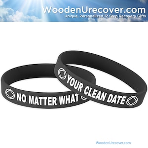 Puede incluir: Dos pulseras de silicona negras con texto blanco y un símbolo. La pulsera superior dice "YOUR CLEAN DATE" y la pulsera inferior dice "NO MATTER WHAT".