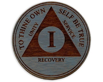 Puede incluir: Una moneda de sobriedad de madera con fondo azul y un triángulo marrón con las palabras "To Thine Own Self Be True" y "Unity, Service, Recovery" inscritas a su alrededor. El centro del triángulo tiene un gran número romano "I" dentro de un círculo.