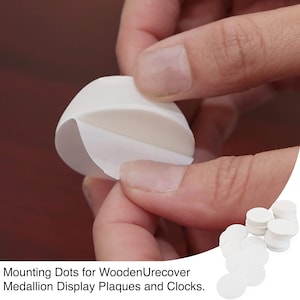 May include: White adhesive mounting dots for wooden plaques and clocks. The dots are shown in a pile and being peeled apart.