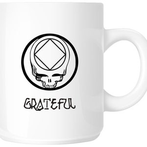 May include: White ceramic mug with a black and white graphic of a skull with a diamond inside a circle. The text "GRATEFUL" is printed below the graphic.
