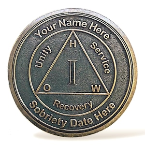 Può includere: Una moneta di sobrietà color bronzo con le parole "Your Name Here" e "Sobriety Date Here" attorno al bordo. Il centro presenta un triangolo con le lettere "H", "I" e "W", e le parole "Unity", "Service" e "Recovery".