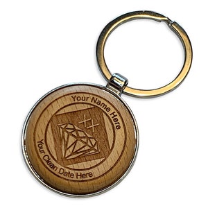 May include: A round wooden keychain with a silver-colored metal rim and a gold-colored key ring. The wooden surface is engraved with a diamond graphic and the text "Your Name Here" and "Your Clean Date Here".