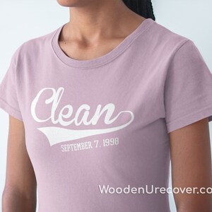 May include: A light pink t-shirt with the word "Clean" in white text with a white baseball-style arc underneath. The text "SEPTEMBER 7, 1990" is below the arc.