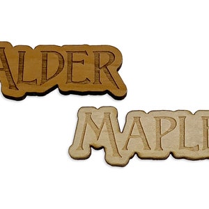 May include: Two wooden signs with the words "Alder" and "Maple" engraved on them. The "Alder" sign is a darker brown color, while the "Maple" sign is a lighter brown color.