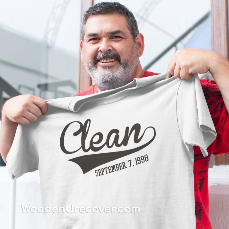 May include: White t-shirt with black text that reads "Clean" in a vintage baseball font. Below the text is "SEPTEMBER 7, 1998". The website "WoodenUrecover.com" is printed at the bottom of the shirt.