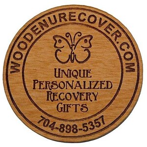 May include: Wooden round coaster with a brown wood grain finish. The coaster has a circle design with the text "WOODENRECOVER.COM" around the outside edge. Inside the circle is a butterfly design and the text "UNIQUE PERSONALIZED RECOVERY GIFTS 704-898-5357".