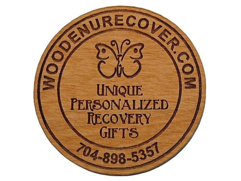 May include: Wooden round coaster with a brown wood grain finish. The coaster has a circle design with the text "WOODENRECOVER.COM" around the outside edge. Inside the circle is a butterfly design and the text "UNIQUE PERSONALIZED RECOVERY GIFTS 704-898-5357".