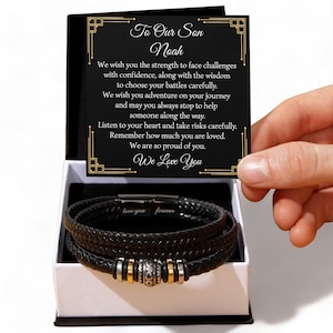 May include: A black leather bracelet with silver and gold details, displayed in a white gift box. The accompanying card reads "To Our Son Noah" with a loving message. The bracelet is inscribed with "love you forever".
