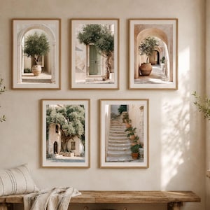May include: A set of five framed wall art prints featuring Mediterranean architectural scenes. The images display stone archways, olive trees in terracotta pots, a green door, and a stone staircase lined with potted plants in neutral beige tones.
