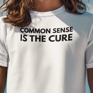 May include: A white t-shirt with black text that reads "COMMON SENSE IS THE CURE".