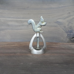 May include: A silver metal nutcracker with a squirrel figurine on top. The squirrel is holding a nut in its paws.