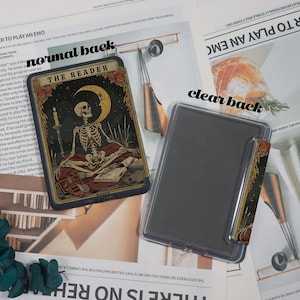 May include: A tarot card featuring a skeleton, a crescent moon, and the text "THE READER" against a dark backdrop. A clear phone case is positioned next to the card, with a small card insert.
