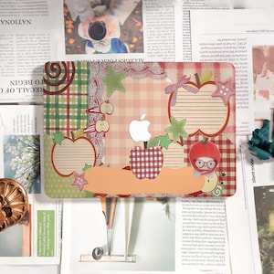 May include: A decorative laptop skin featuring an apple theme. The design includes apple shapes, stars, and a gingham pattern in red, green, and orange. The skin is placed on a newspaper background.