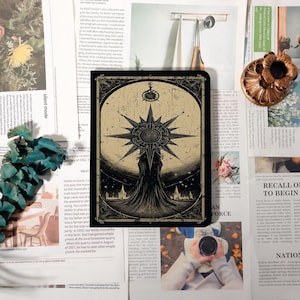 May include: A black and beige rectangular art print featuring a detailed illustration of a starburst design with two figures below. The artwork has a vintage aesthetic, with a celestial theme. The print is surrounded by newspaper clippings.