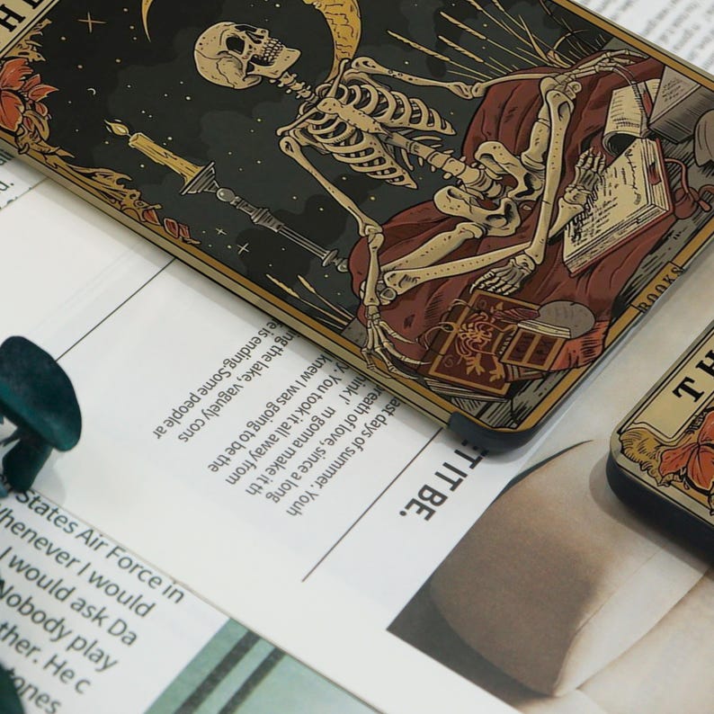 May include: A tarot card depicting a skeleton resting on a burgundy cushion, surrounded by books and a candle. The card has a dark background with a crescent moon and stars. Part of a tarot deck.