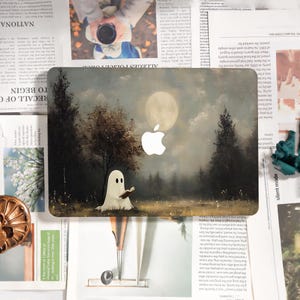 May include: Laptop case featuring a whimsical illustration of a ghost reading a book in a moonlit forest. The design incorporates a full moon and trees, with the Apple logo integrated into the artwork. The case has a matte finish.