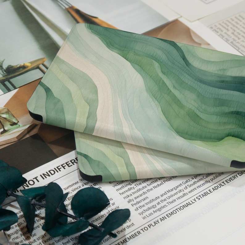 K&ouml;nnte beinhalten: Eine Handyh&uuml;lle mit einem Aquarelldesign in Gr&uuml;n- und Wei&szlig;t&ouml;nen. Das Design hat ein wellenf&ouml;rmiges Muster, mit dunklerem Gr&uuml;n oben und helleren Farbt&ouml;nen unten. Die H&uuml;lle hat schwarze Ecken.