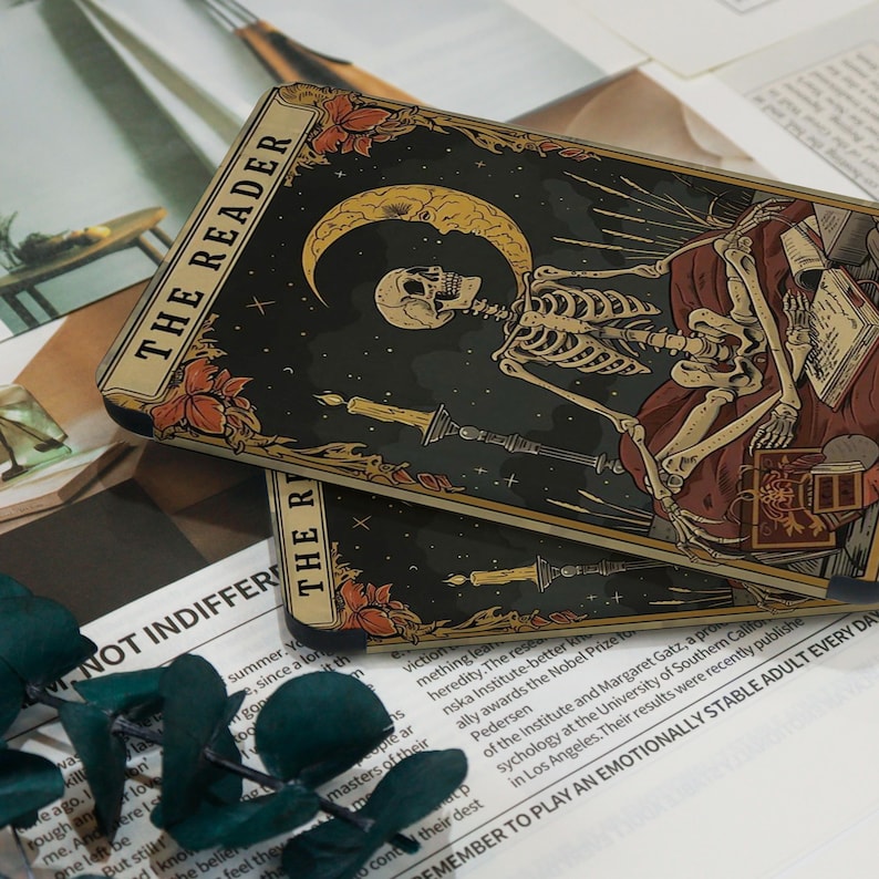 May include: Two tarot cards titled "THE READER" are shown. The cards depict a skeleton figure with a crescent moon, candles, and floral details. The background is dark with stars.