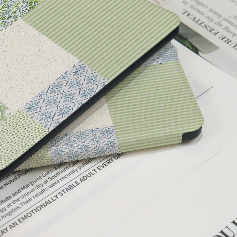 May include: Close-up of two notebooks with a patchwork design. The covers feature various patterns, including floral, striped, and dotted designs in shades of green, blue, and cream. The notebooks have black edges and are resting on a white surface with text.