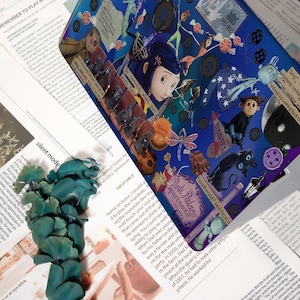 May include: A vibrant, detailed illustration featuring characters and elements from a fantasy movie. The artwork is set against a dark blue background with text and various objects, including buttons, a black cat, and a dragonfly. The words "Be careful what you wish for" are visible.