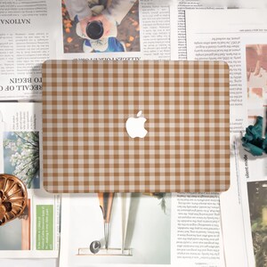May include: A brown and beige checkered laptop skin with the Apple logo in the center. The skin is rectangular and covers the top of the laptop. The background is a newspaper.