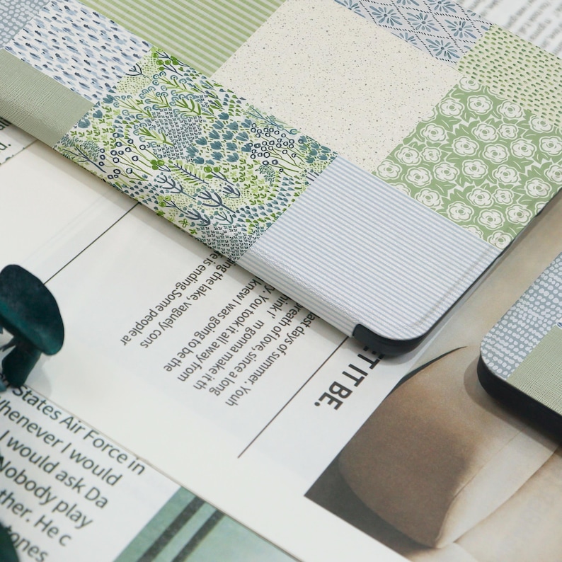 May include: A close-up of a patchwork-style laptop case with a variety of green and blue floral and patterned fabrics. The case is resting on a newspaper with text. The edges of the case are black.