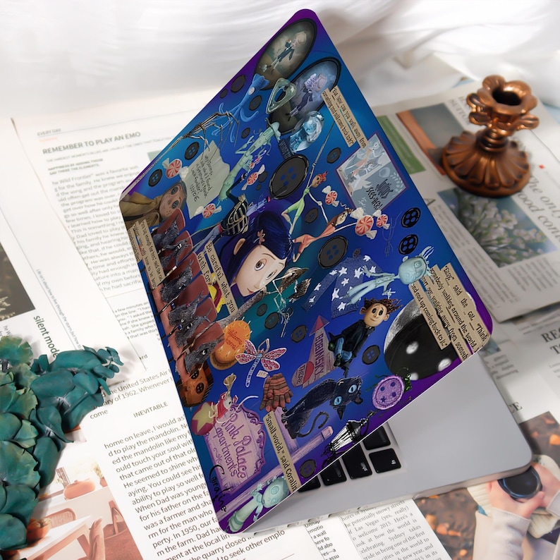 May include: A laptop skin featuring a collage of illustrations and text from the animated film, "Coraline." The design is predominantly blue with images of characters, buttons, and other elements from the movie. The text includes phrases like "Pink Palace apartments" and "Be careful what you wish for."