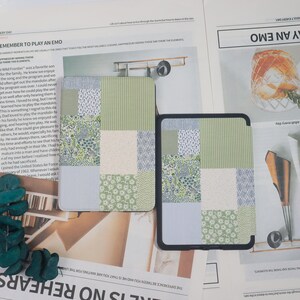 May include: Two patterned tablet cases. One is a patchwork design with green, white, and blue floral and striped patterns. The other case is black with a similar patchwork design. The cases are on a newspaper background.