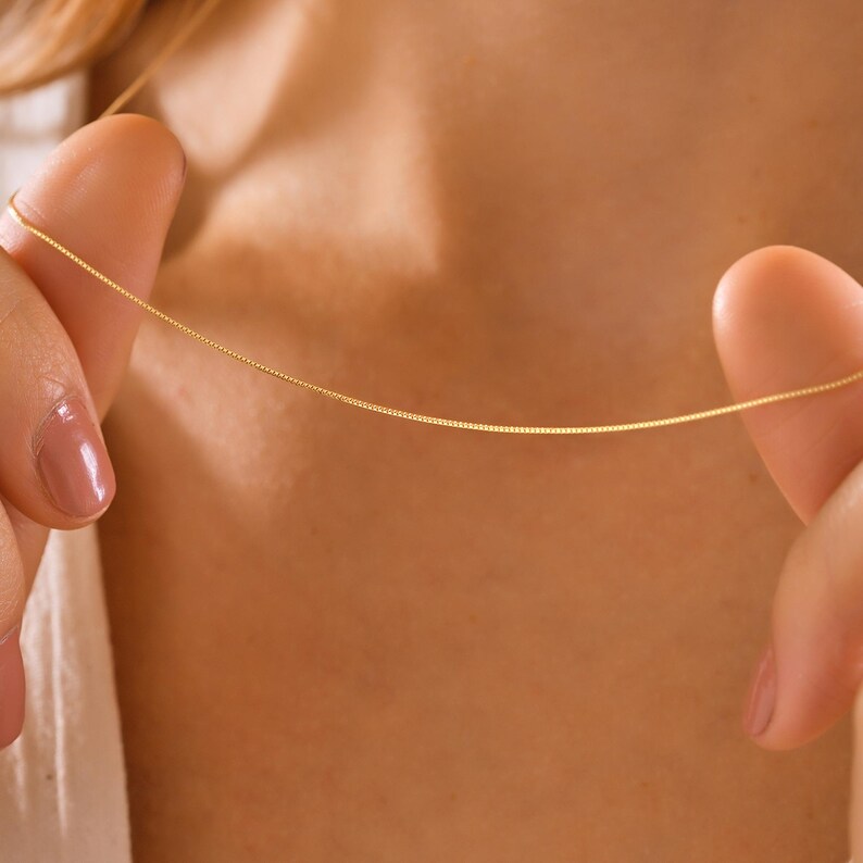 May include: A delicate gold chain necklace, shown being held by a person's fingers.