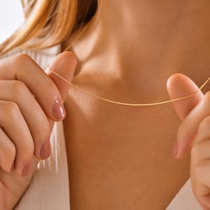 May include: A delicate gold chain necklace worn by a person. The chain is thin and has a subtle shine.
