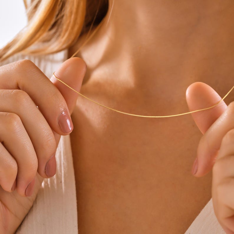 May include: A delicate gold chain necklace worn by a person. The chain is thin and has a subtle shine.
