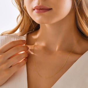 May include: A delicate gold chain necklace worn by a person. The chain is thin and has a subtle shine.