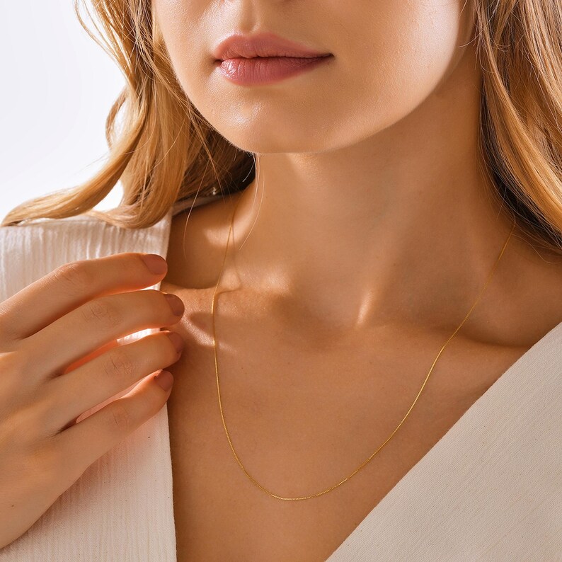May include: A delicate gold chain necklace worn by a person. The chain is thin and has a subtle shine.