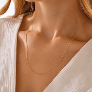 May include: A delicate gold chain necklace, worn on a person's neck. The chain is thin and has a subtle shine.