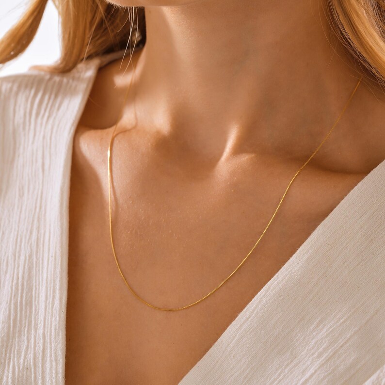 May include: A delicate gold chain necklace, worn on a person's neck. The chain is thin and has a subtle shine.