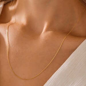 May include: A delicate gold chain necklace worn on a person's neck. The chain is thin and has a subtle shine.