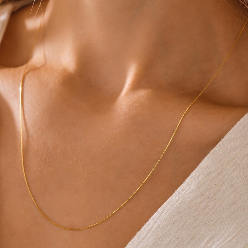 May include: A delicate gold chain necklace worn on a person's neck. The chain is thin and has a subtle shine.