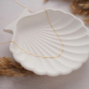 May include: A delicate gold chain necklace displayed on a white seashell background.