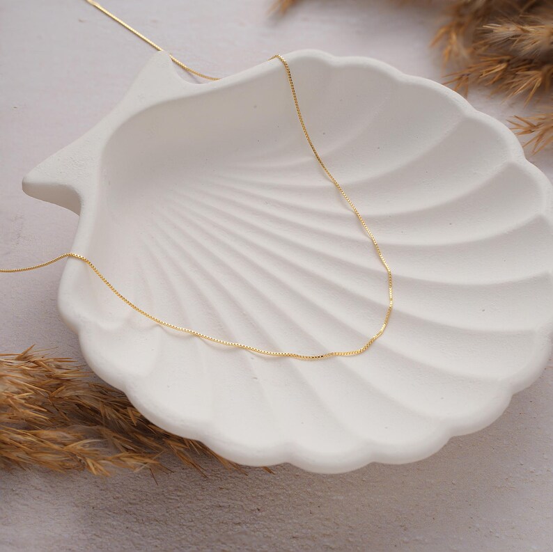 May include: A delicate gold chain necklace displayed on a white seashell background.