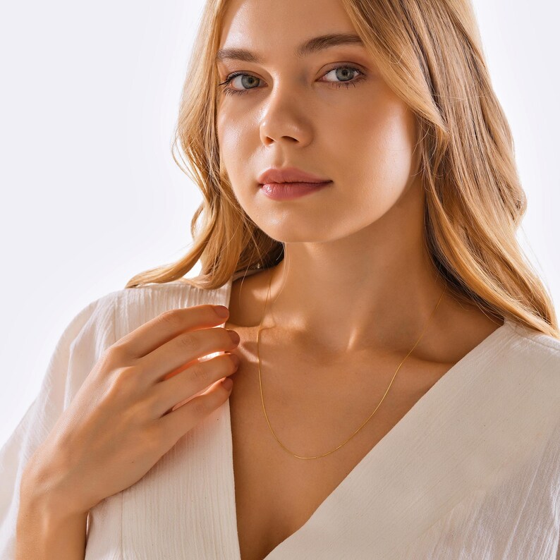 May include: A delicate gold chain necklace worn by a person with long blonde hair. The chain is thin and has a subtle shine.