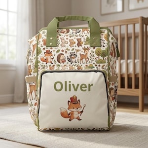 Op de afbeelding: Een rugzak met een crèmekleurige basis en een herhalend patroon van bosdieren zoals vossen, herten en wasberen. Het voorvak toont de naam Oliver in groene tekst boven een enkele illustratie van een vos die een hoedje draagt.