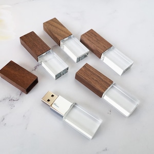 May include: Five wooden USB flash drives with clear crystal tops. The drives are arranged in a semi-circle on a white marble surface.