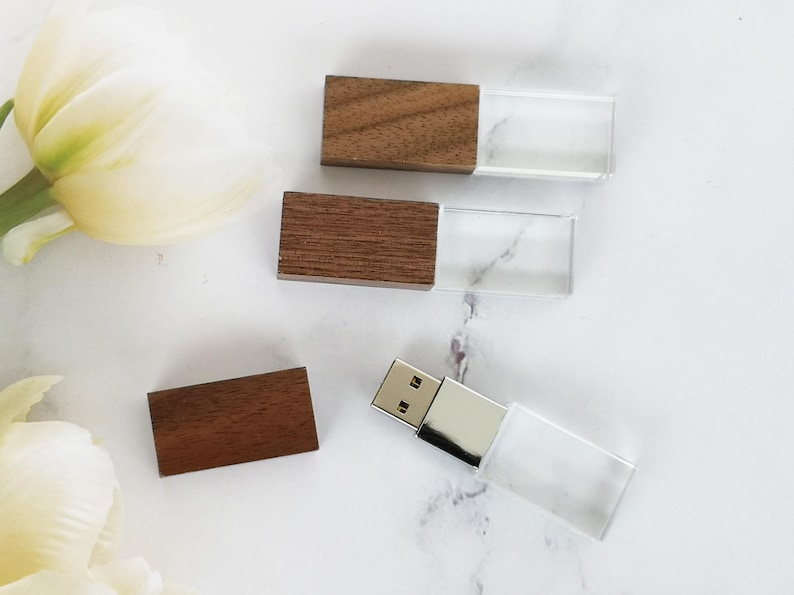 May include: Three wooden USB flash drives with clear plastic casings. The drives are arranged on a white marble surface.